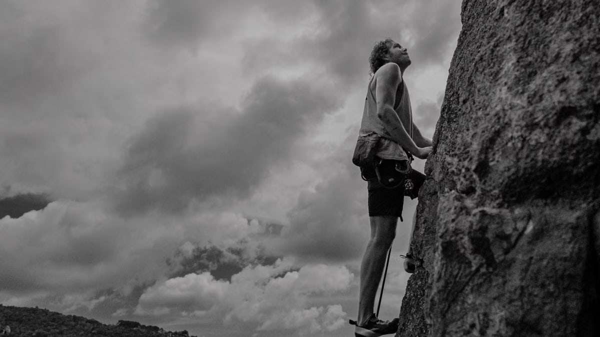 Adventurous man rock climbing, looking up against a cloudy sky, in a black and white setting.
