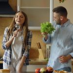 Attractive young joyful couple have fun dancing and singing while cooking in the kitchen at home in the morining