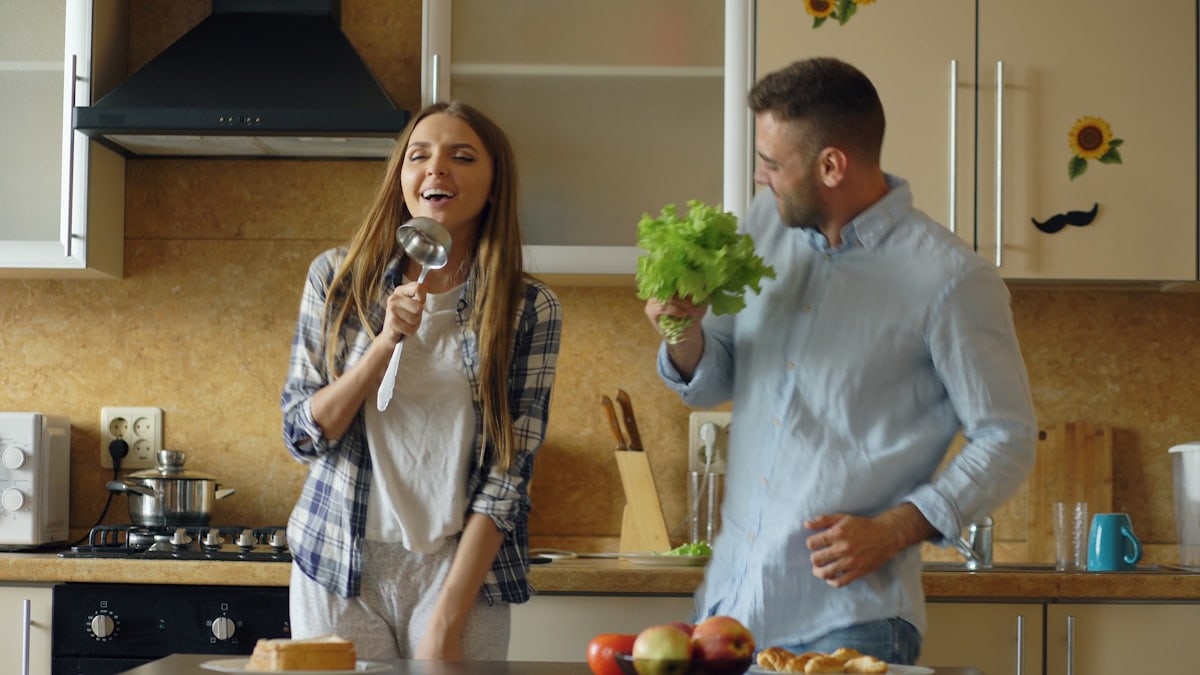 Attractive young joyful couple have fun dancing and singing while cooking in the kitchen at home in the morining